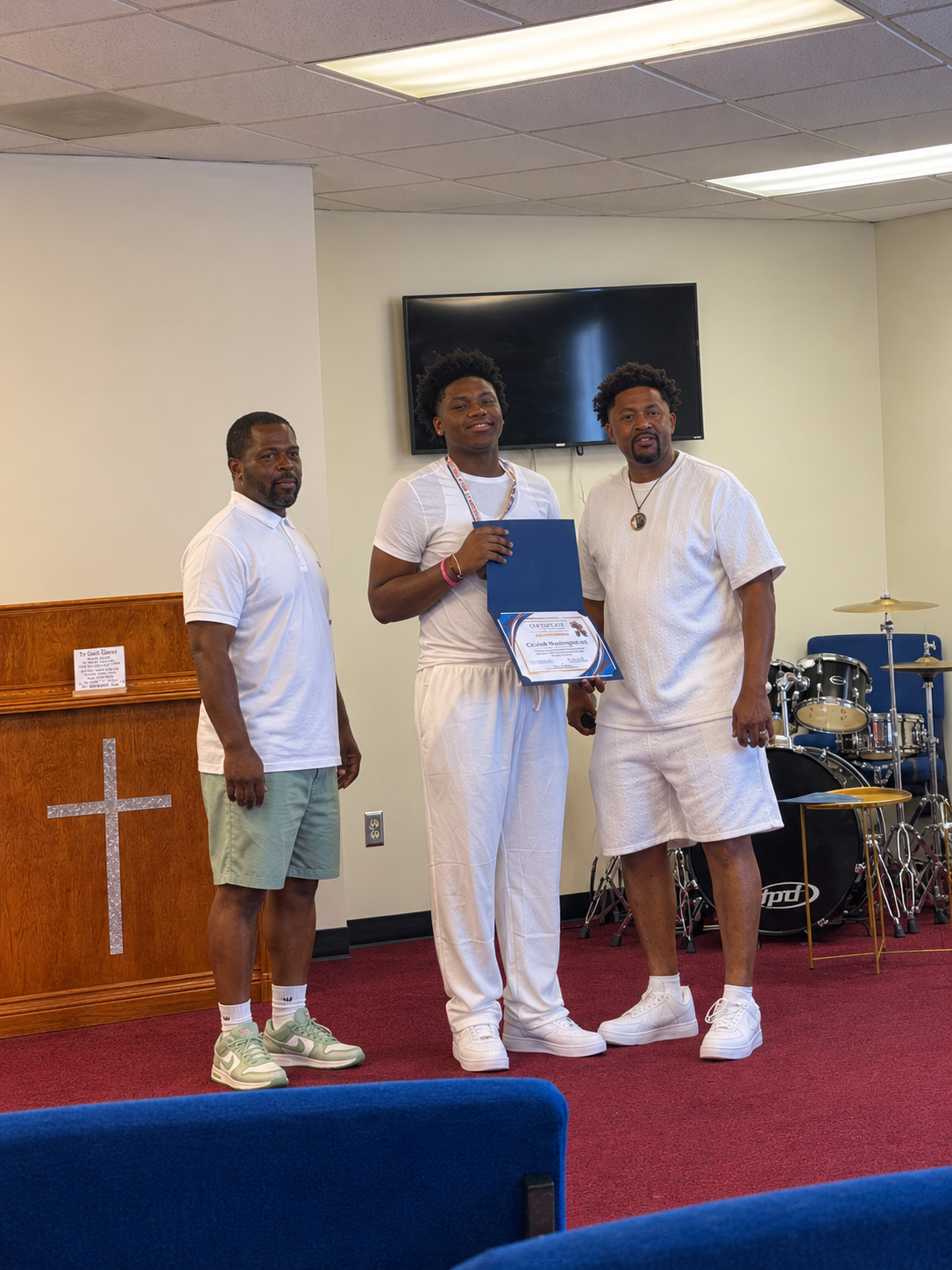 An alumnus smiles while holding his certificate between two mentors