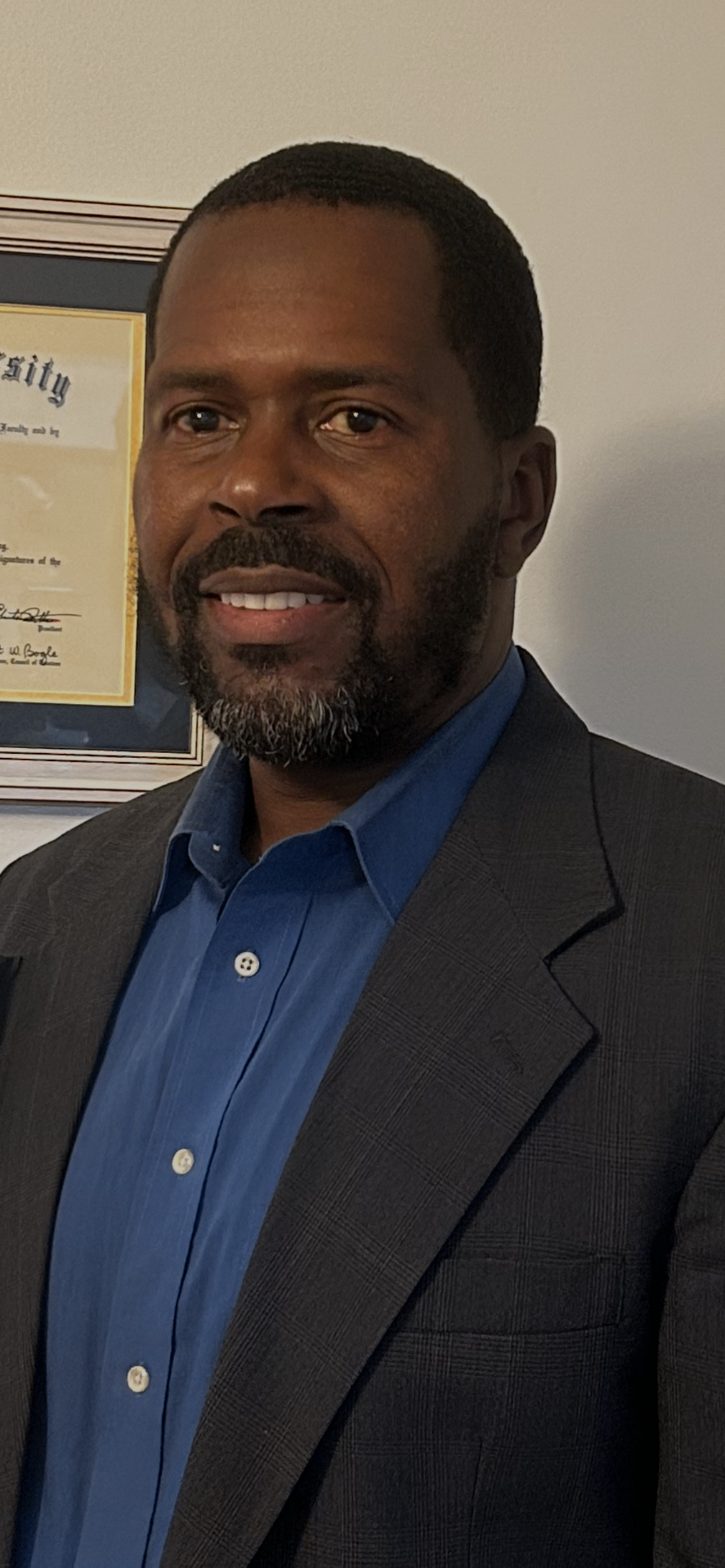 Portrait of Dr. Jermane Miller, Ed.D., smiling in a dark blazer and blue shirt